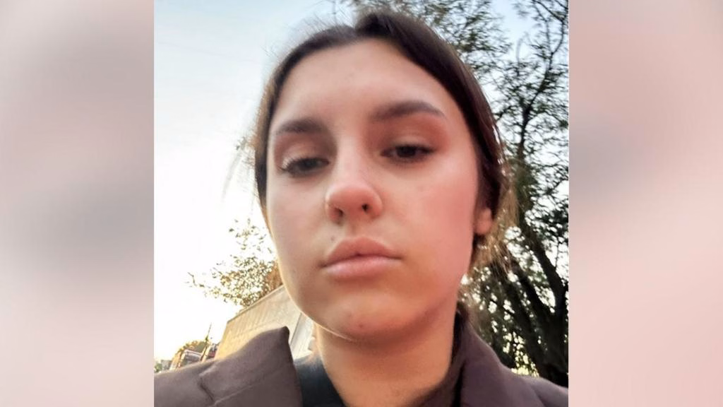 A close up of a young woman's face, as she stands outside with a tree in the background