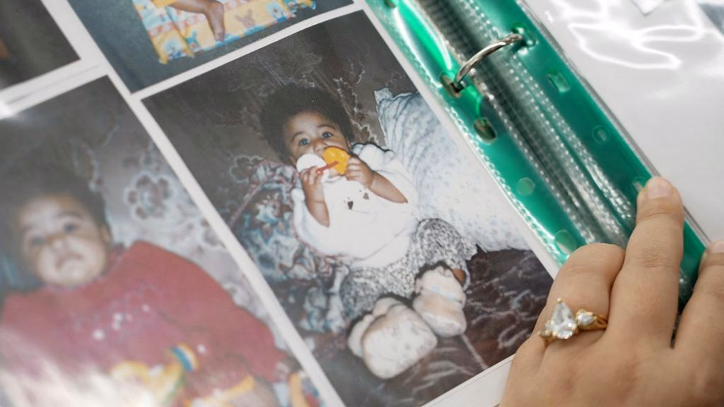 A hand opens the page of a photo album with pictures of a baby girl